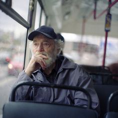 an old man sitting on a bus with his hand under his chin and looking out the window