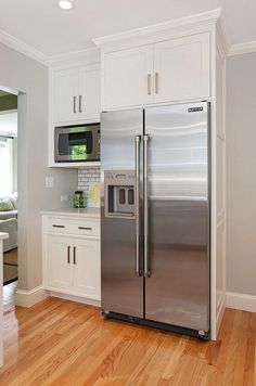 a silver refrigerator freezer sitting inside of a kitchen next to white cabinets and wooden floors