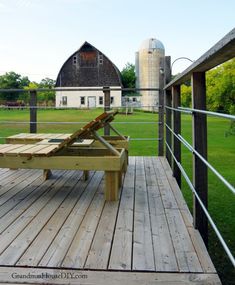 a wooden bench sitting on top of a wooden deck in front of a barn and silo