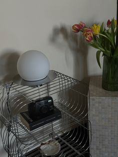 a white lamp sitting on top of a metal shelf next to a vase with flowers