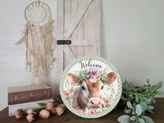 a plate with a cow painted on it sitting next to some flowers and books near a door