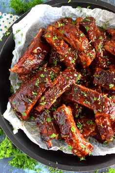 bbq ribs with barbecue sauce and parsley in a black pan on a blue tablecloth