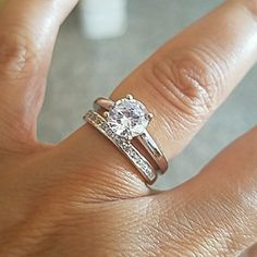 a woman's hand with a diamond ring on top of her finger and the other hand holding an engagement ring