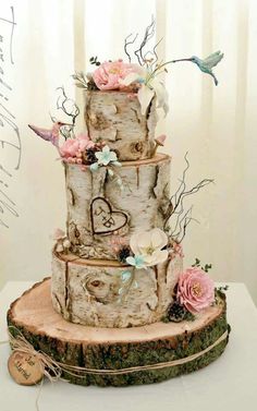 a three tiered wedding cake decorated with flowers and hearts on a tree stump stand