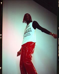 a man with dreadlocks is wearing red pants and a white t - shirt