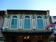 an old building with blue shutters and american flag on the front door in front of it