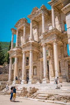 some people are standing in front of an old building with many pillars and columns on it