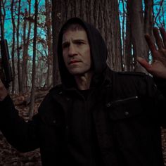 a man in a hooded jacket holding up his hand and looking at the camera with an evil look on his face