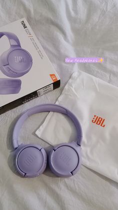 purple jbl headphones sitting on top of a bed next to a white bag