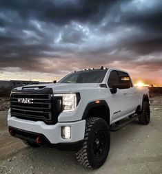 a white truck parked on top of a dirt field under a cloudy sky at sunset