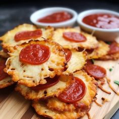 small pizzas with pepperoni and cheese on a cutting board next to dipping sauce