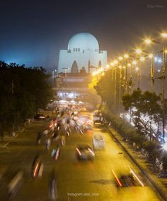 many cars are driving down the street at night with city lights in the back ground