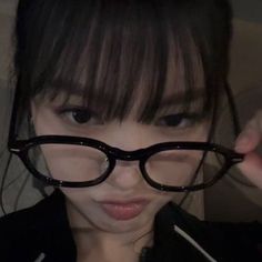 a girl with glasses on her face looking at the camera while she is holding something in front of her eye