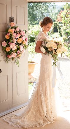 a woman in a wedding dress holding a bouquet and looking at the camera while standing next to an open door