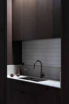 a kitchen with dark wood cabinets and white counter tops is seen from the doorway to the sink area