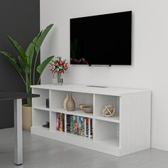 a television mounted on the wall above a white book shelf with books and vases