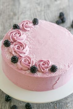 a cake with pink frosting and blackberries is on a white plate next to berries