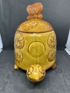 a yellow ceramic container with an ornate design on the top and bottom, sitting on a gray surface