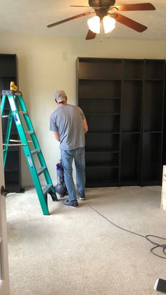 a man standing on top of a step ladder in a room with black bookcases