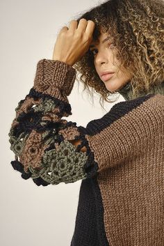 a woman with curly hair wearing a brown and black sweater holding her hands on her head