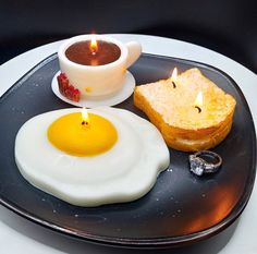 an egg, toast and sauce on a black plate with a lit candle in the middle