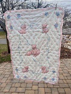 a pink teddy bear quilt hanging from a clothes line on a brick walkway in front of a house