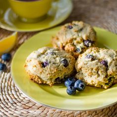 three blueberry muffins on a yellow plate next to a cup of coffee