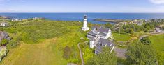 an aerial view of a lighthouse surrounded by trees and houses near the ocean with blue sky