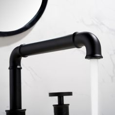 two black faucets are in front of a white wall with a round mirror