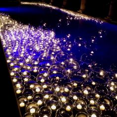 rows of lit candles are lined up along the edge of a swimming pool at night