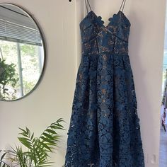 a blue dress hanging on a wall in front of a mirror and potted plant