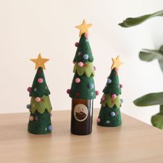 three small christmas trees sitting on top of a wooden table next to a wine bottle