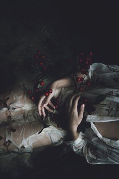 a woman laying on top of a bed covered in red berries next to her hands