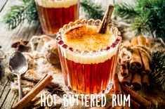 two glasses filled with hot buttered rum surrounded by cinnamon sticks and christmas greenery