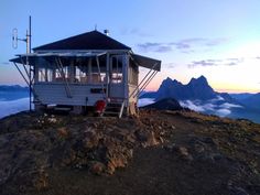 a small white building on top of a hill with mountains in the background at sunset