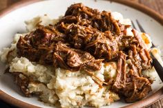 a white plate topped with mashed potatoes covered in shredded beef and gravy