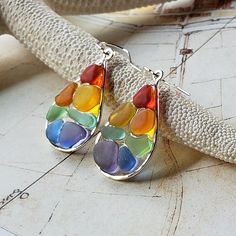 a pair of multicolored glass tear earrings sitting on top of a white surface