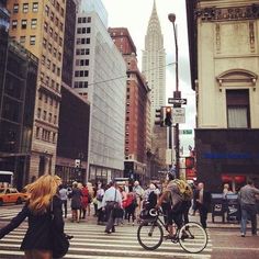 people walking and riding bikes on a city street with tall buildings in the back ground