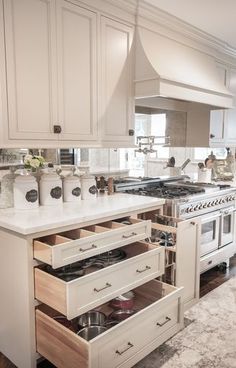 an open drawer in the middle of a kitchen with white cabinets and marble counter tops