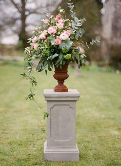 a vase filled with flowers sitting on top of a cement pillar in the middle of a field