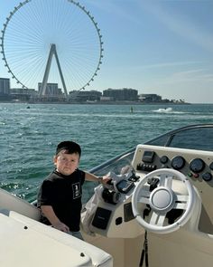 a young boy sitting on the front of a boat in the water near a ferris wheel