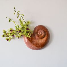 a vase filled with flowers sitting on top of a white wall next to a brown snail