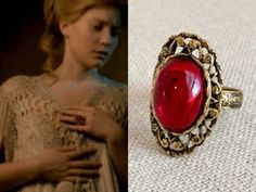 a close up of a ring with a red stone in the middle and an image of a woman wearing a dress