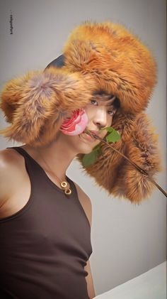 a woman wearing a fur hat with flowers on it's head and holding a rose in her mouth