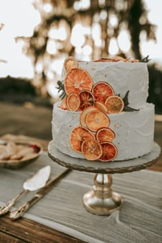 a white cake with orange slices on it sitting on a table next to silverware