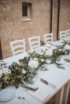 the table is set with white flowers and greenery