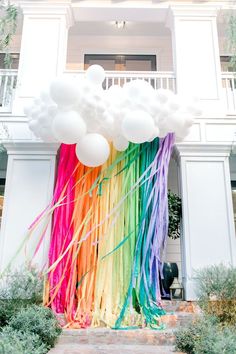 a rainbow colored streamer with white balloons in front of a building