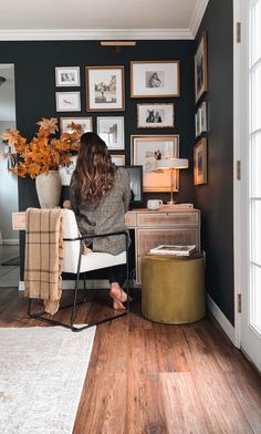 a woman sitting in a chair with her back to the camera and looking at pictures on the wall