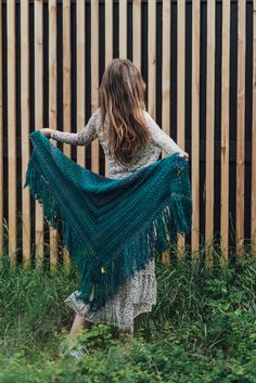 a woman holding a green shawl in front of a wooden fence with tall grass