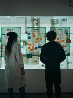 two people standing in front of a wall with papers on it